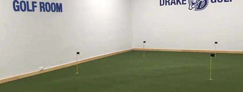 indoor putting green with many pins and holes. the wall displays text "zach johnson golf room" and "drake golf" with logos
