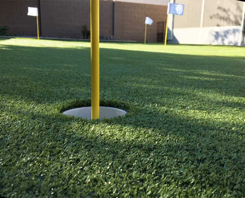close up ground view of a cup and pin on an artificial putting grass course