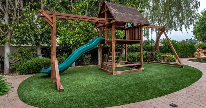 residential backyard small wooden playground installed onto artificial turf grass