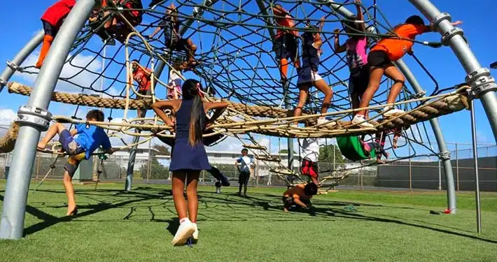 group of children happily playing on rope monkey bars on synthetic playground grass