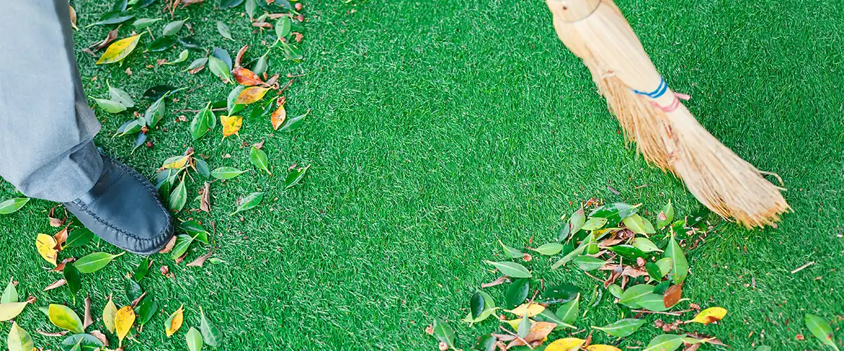 close up of person cleaning artificial grass debris with a broom.