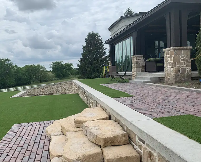 beautiful artificial grass landscaping outside of a large house. the ground is flat with a multi-layer landscaping design and rocks and bricks.